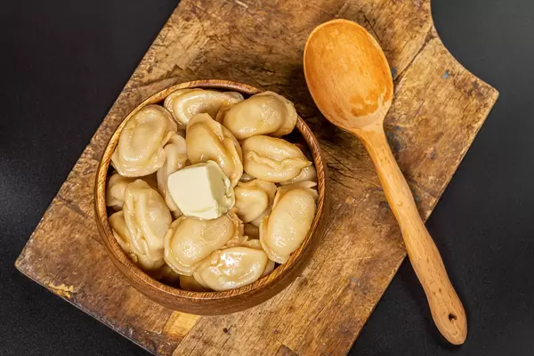 Boiled dumplings with butter on a dark background with a wooden spoon, top view