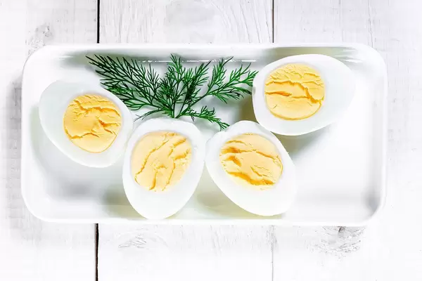 Boiled eggs cut on a plate with dill leaves on a white wooden background