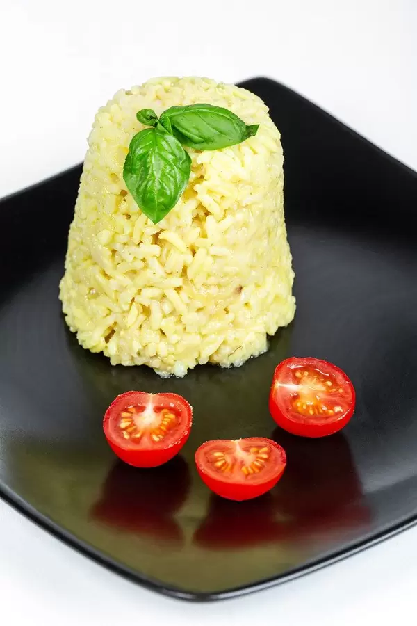 Boiled rice with slices of tomatoes and basil leaves on a black plate