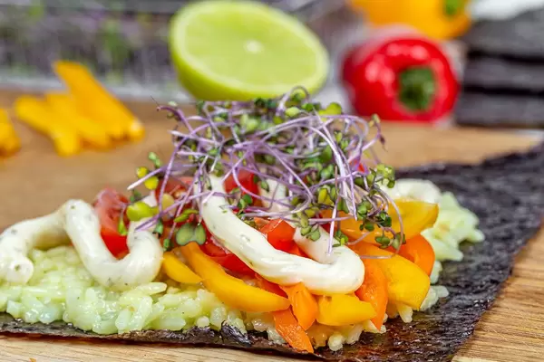 Boiled rice with vegetables, micro-greens and sauce on a nori leaf, close-up