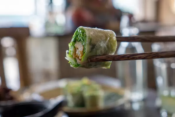 Bokeh Food Photo of Chopsticks holding a Piece of Goi Cuon - Vietnamese Summer Rolls in a Restaurant in Vietnam