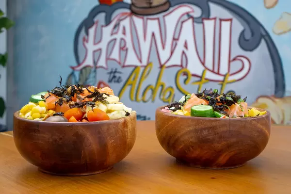 Bokeh Food Photo of two Healthy Poke Bowls with different Ingredients on a Wooden Table with Hawaii the Aloha State Drawing in the Background