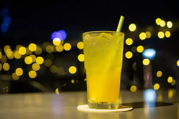 Bokeh Foto von einem Maracuja Mocktail mit Eiswürfel und Zitronengras Strohhalm in einem Cocktail Glas mit Lichtern im Hintergrund in einer Rooftop Bar