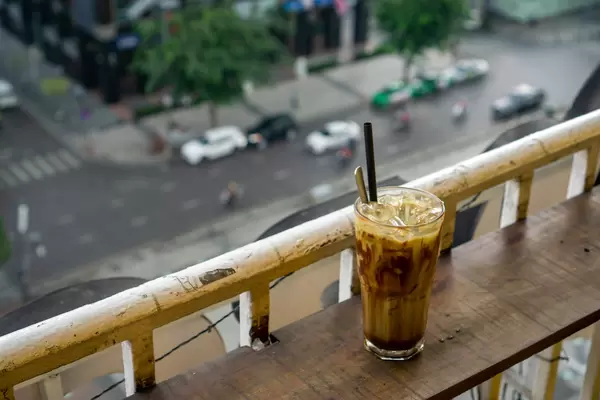 Bokeh Photo of Cold Chocolate Drink with Plastic Straw and Spoon on a Balcony of a Coffee Shop looking down on the Streets