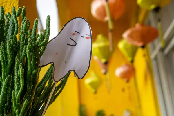 Bokeh Photo of Paper Ghost Halloween Decorations in a Mini Cactus with Hanging Lanterns in the Background