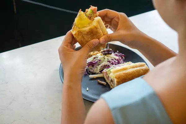 Bokeh Photo of Person eating a Pulled Pork Sandwich with Swiss Cheese, Ham and Vegetables in a Restaurant