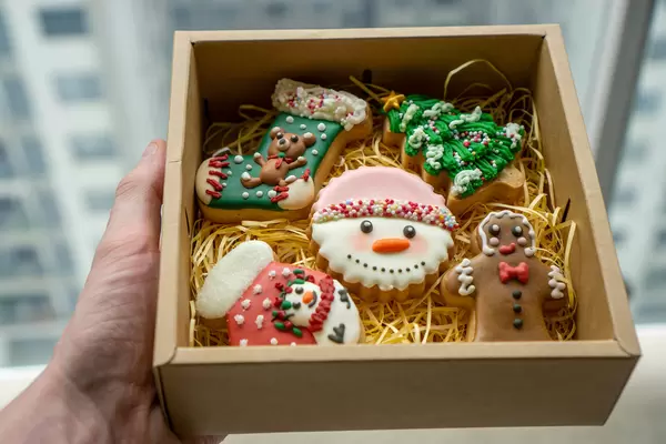 Bokeh Photo of Person holding a Paper Gift Box with Christmas Gingerbread Cookies in Different Christmas Theme Designs