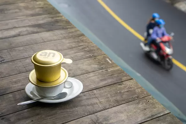 Bokeh Photo of Vietnamese Hot Coffee on a Wooden Table with a Motorbike driving past on the Street