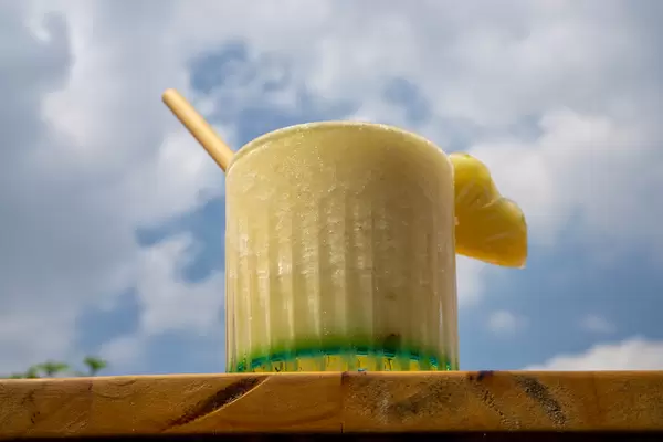 Bokeh Photo of Virgin Pina Colada Mocktail with Bamboo Straw and Fresh Pineapple with Cloudy Blue Sky in the Background