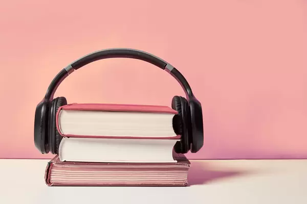 Books and modern headphones on light pink background, space for text
