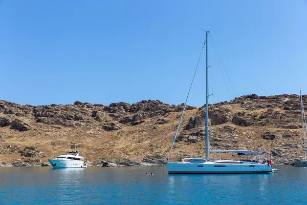 Boote legen in der Bucht vor Kolimpithres, Paros - Griechenland, an und Urlauber schwimmen vor der felsigen Küste im Mittelmeer
