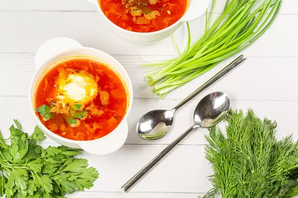 Borscht with sour cream and herbs on a white wooden background