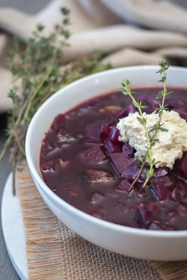 Borschtsch Suppe aus Rotkohl, Suppenfleisch und Kartoffeln dekoriert mit Rosmarin in weißer Schüssel