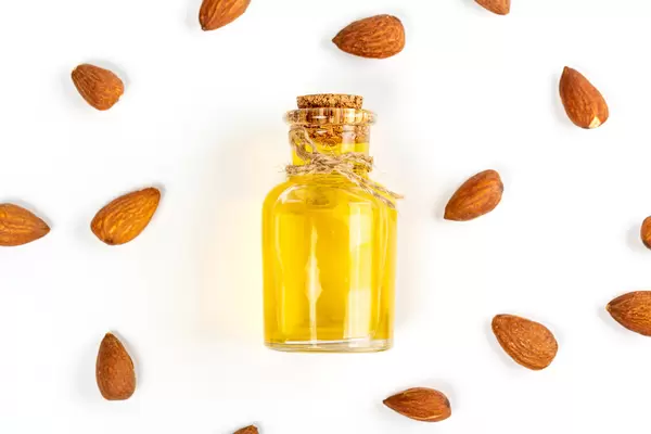 Bottle of almond oil and almonds on white background, top view