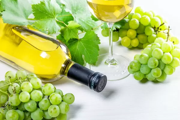 Bottle of white wine, glass, green grapes and leaves on white table (Flip 2019)