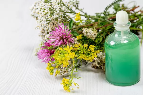 Bottle with green cosmetic and a bouquet of wild flowers on a white wooden background. The concept of natural cosmetics (Flip 2019)