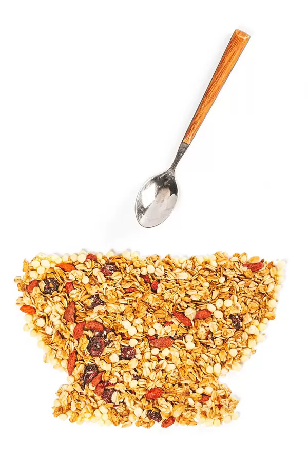 Bowl made of oatmeal with dried berries and seeds on a white background with a spoon, top view