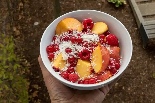 Bowl mit Himbeeren, Johannisbeeren, Pfirsich und Kokosraspeln