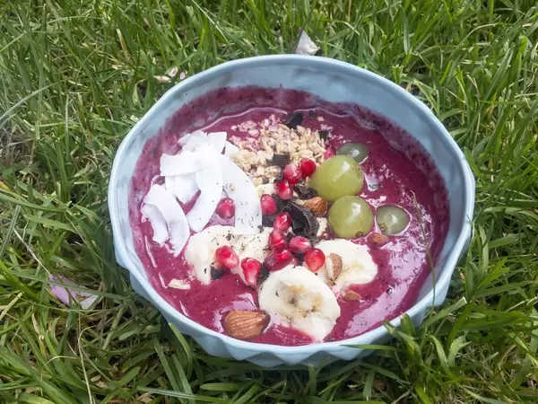 Bowl mit Kokos-Chips, Bananen, Mandeln, Granola, Granatapfelkernen und selbst gehobelter dunkle Schokolade