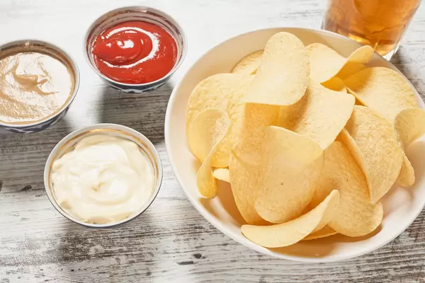 Bowl of crispy potato chips, sauces and glass of beer on the wooden table
