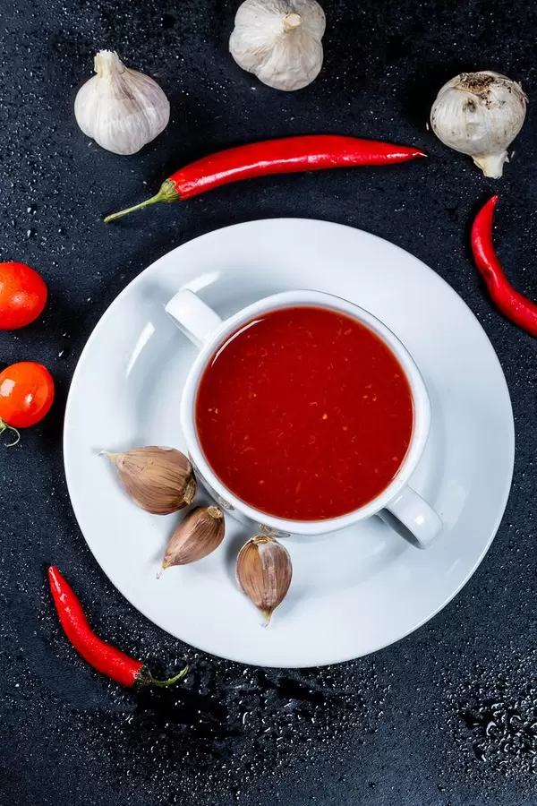 Bowl of fresh homemade tomato soup and spice on black table, top view