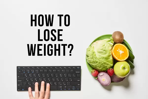 Bowl of fruits and vegetables, and hand of person typing on computer keyboard with text - how to lose weight
