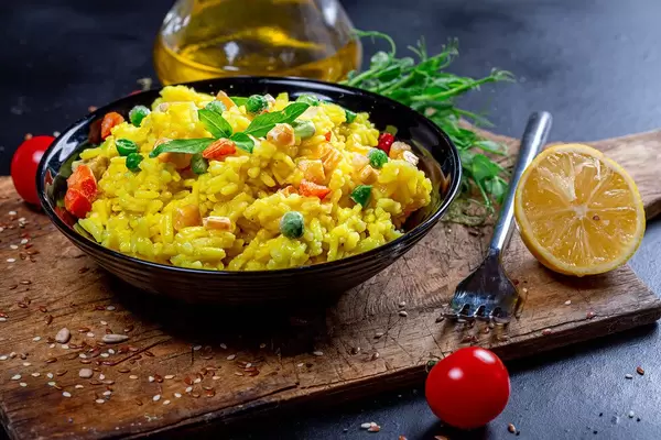 Bowl of yellow rice with vegetables and greens on a dark background with olive oil, tomatoes and seeds (Flip 2019)