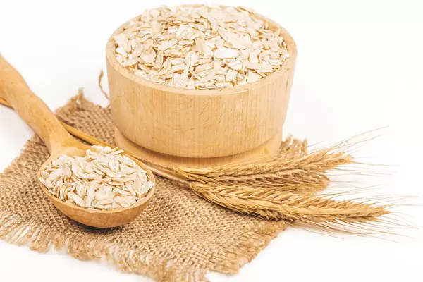 Bowl with raw oatmeal on white background with spikelets
