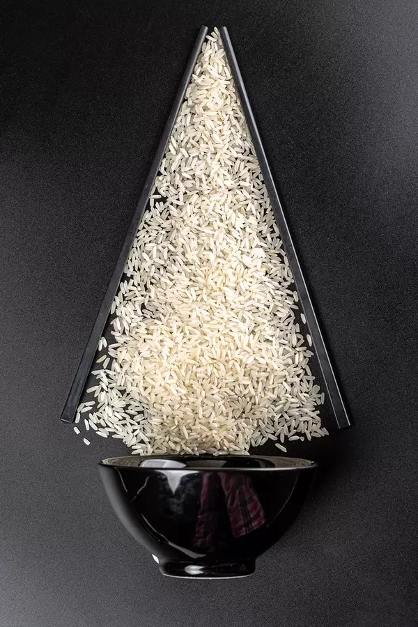 Bowl with raw rice and chopsticks on a dark background, top view