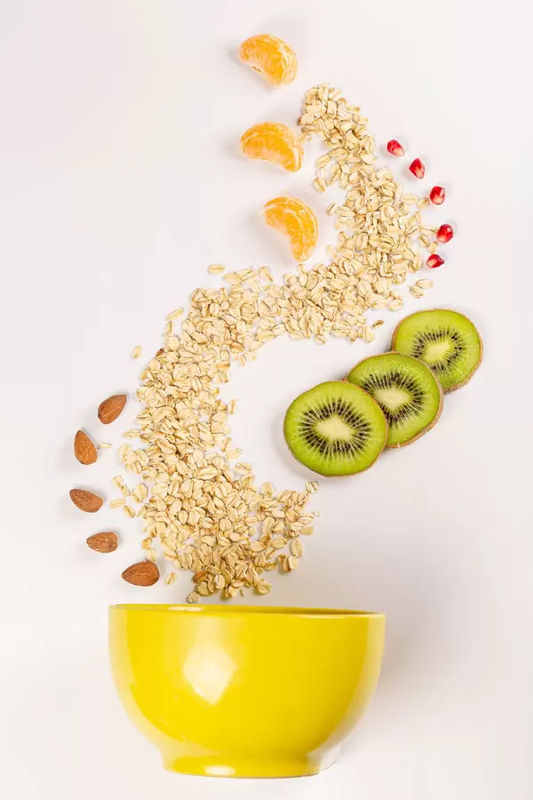 Bowl with sprinkled oatmeal, almonds, kiwi, tangerine and pomegranate, top view