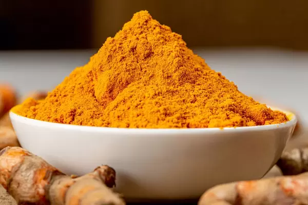 Bowl with turmeric close-up on a dark background with fresh turmeric roots (Flip 2020)