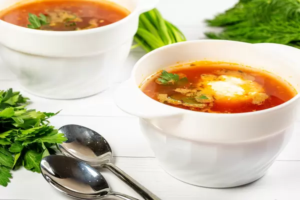 Bowls of borscht on the white wooden table with greens