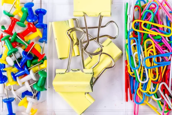 Box mit Büroutensilien wie Reißzwecken, Papierclips und bunten Büroklammern