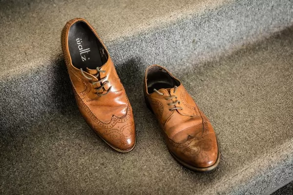 Braune, lederne Schuhe des Bräutigams stehen auf mit Teppich überzogener Treppe