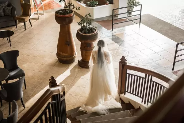 Braut in weißem Kleid und mit Schleier schreitet Holztreppe hinunter in Halle des Zaycoland Hotels
