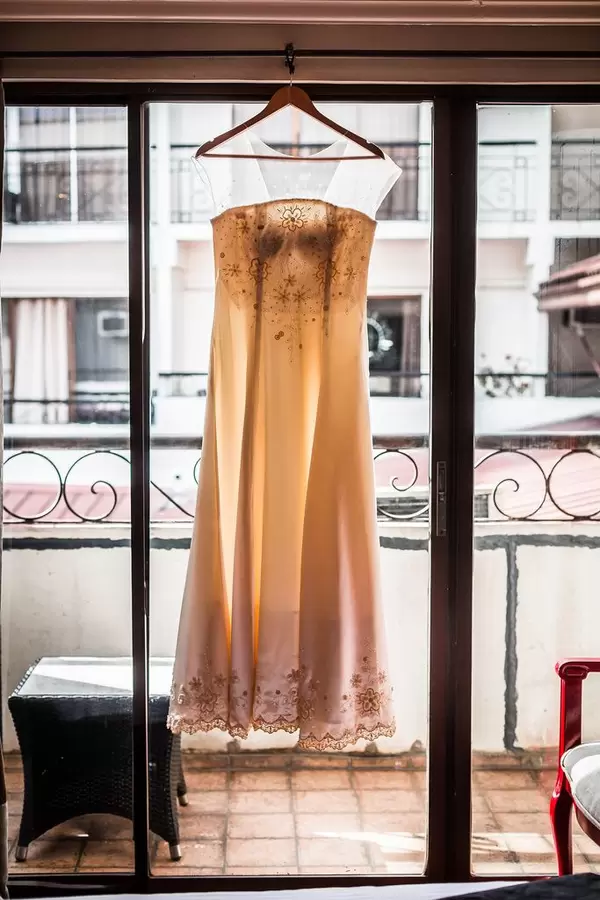 Brautkleid hängt an Fenster vor Balkon im Altbau-Stil – Lichteinfall durch Scheibe schimmert durch Kleid