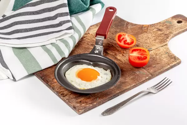 Breakfast background with fried egg in a frying pan with tomato slices