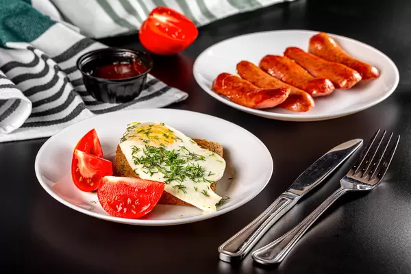 Breakfast background with fried eggs, sausages, bread and sliced tomato