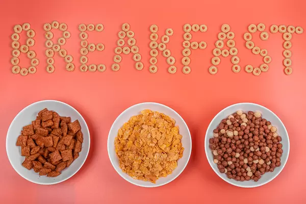 Breakfast background with three bowls of ready-made breakfast corn on pink backdrop, top view