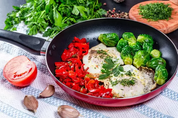 Breakfast in the pan-fried eggs with vegetables and herbs on the table