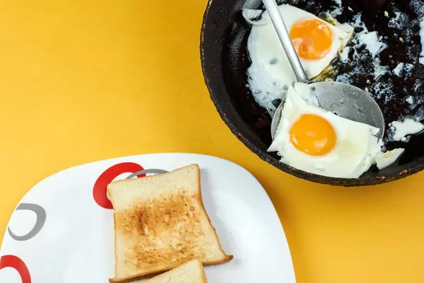 Breakfast preparing process. Putting fried sunny-side-up eggs on to the toasted bread