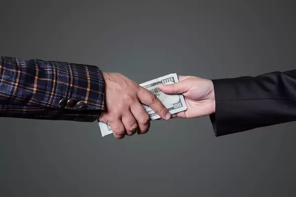 Bribe. Close-up of hands giving money over gray background