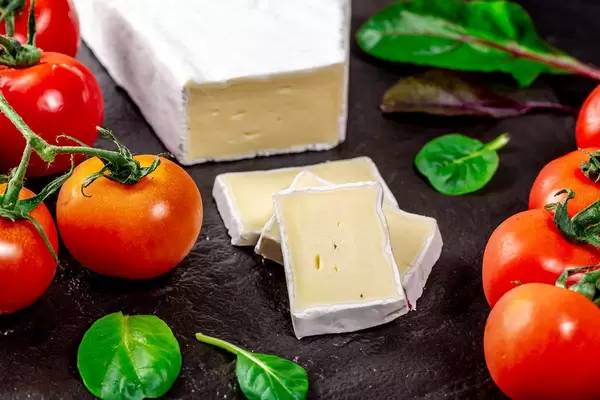 Brie-Käse mit Kräutern und Kirschtomaten auf einer schwarzen Schieferplatte
