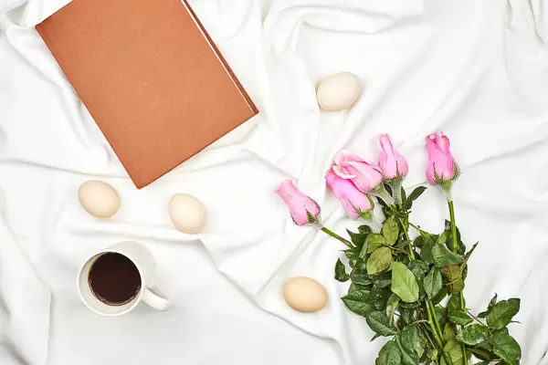 Bright spring background with easter eggs, rose flowers and a cup of coffee