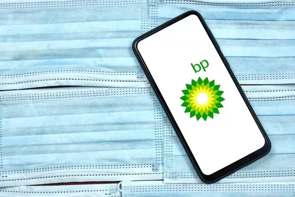 British Petroleum company logo on smartphone screen over the face masks. Global company during coronavirus crisis