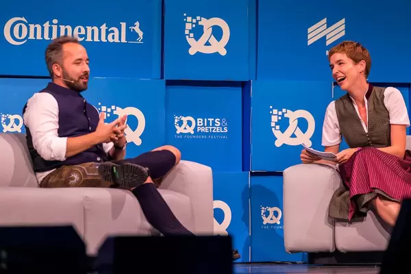 Britta Weddeling lächelt und Drew Houston erzählt seine Geschichte als Dropbox-Gründer auf der Bühne von Bits und Pretzels
