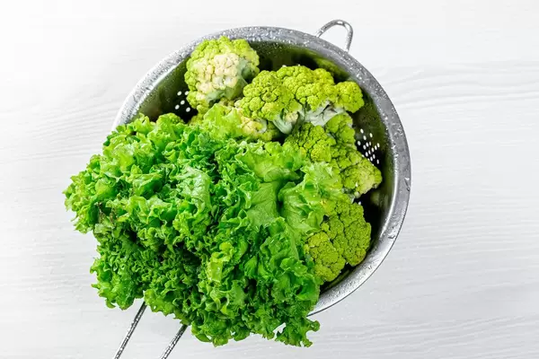 Broccoli and lettuce with water drops in a sieve. Top view