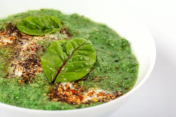 Broccoli cream soup in a bowl with mangold leaves and spices, close-up