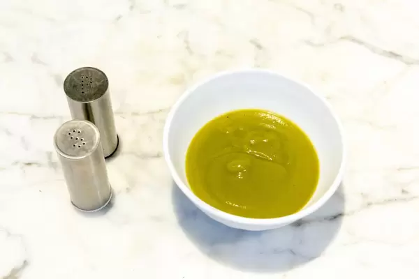 Broccoli creme-soup in a white bowl on a granit table with salt and pepper scatterer