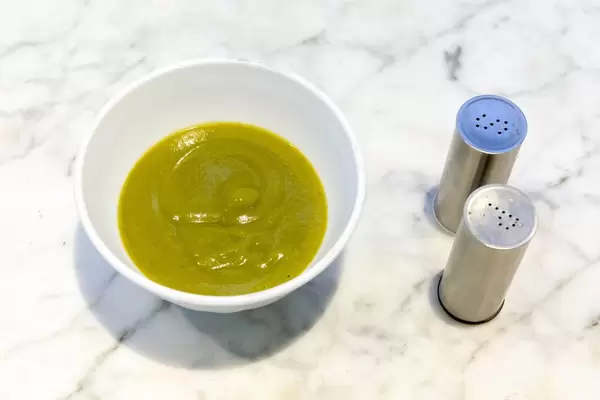 Broccoli Creme-Suppe in einer weißen Schüssel auf Marmortisch mit Salz und Pfefferstreuer